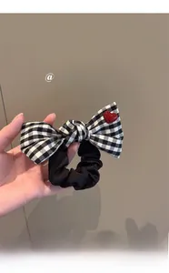 Detail of checkered bow hair tie featuring a bright red heart charm and black scrunchie