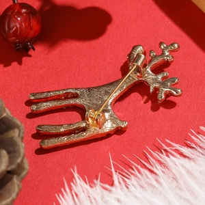 Broche renne dorée avec cristaux sur fond rouge festif avec des pommes de pin