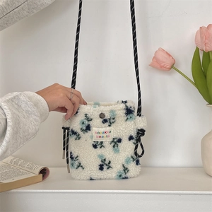 Close-up of white plush floral crossbody bag with woven strap and logo label