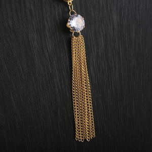 Macro shot of long gold tassel pendant with round clear zircon on black background