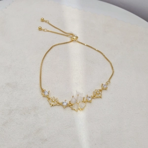 Detail of adjustable gold chain bracelet with white flower charm and sparkling zircons