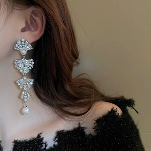 Detail of elegant bow tassel earrings with sparkling rhinestones and pearls on a model
