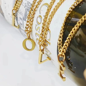 Detalle macro de colgantes de letras LOVE en acero inoxidable oro 14K sobre una botella