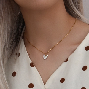Detailed view of a gold chain necklace with a white butterfly pendant worn by a model