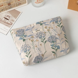 Dettaglio trousse trucco beige con ricami di ortensie blu e trama in seta lucida