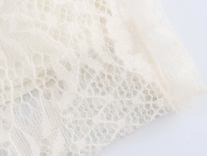 Detailansicht von weißem Blumen-Spitzenstoff mit feiner Netzstruktur am Kleid