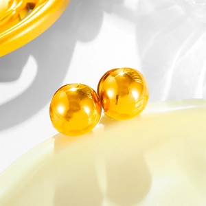 Macro shot of polished gold ball stud earrings reflecting light on a warm ceramic edge