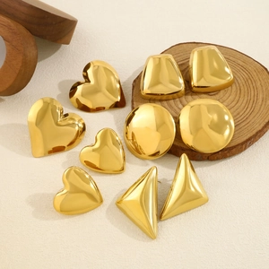 Polished 18K gold heart and geometric stud earrings set on a natural wood stand
