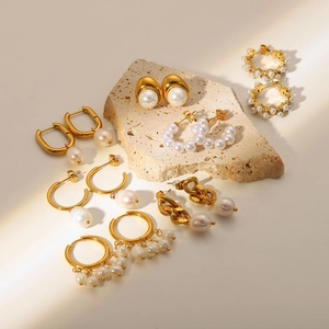 Detailed collection of 18K gold stainless steel pearl earrings on a beige stone base