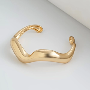 Detailed view of an irregular wavy gold open bangle with a polished sculptural finish