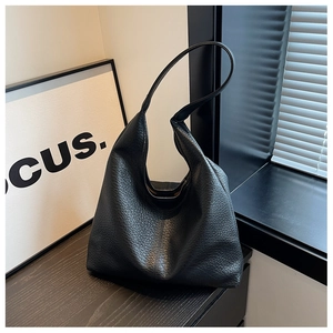 Detail of black lychee grain PU leather tote bag with wide shoulder strap under soft light