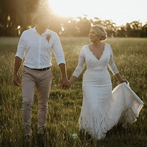 Romantic white lace V-neck wedding dress with long sleeves in outdoor sunset scenery