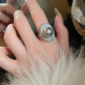 Close-up of a silver oval ring with a gray pearl and double pavé diamond halo on model