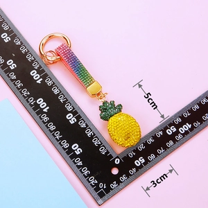 Detailed view showing a 5cm x 3cm pineapple keychain with yellow and green rhinestones