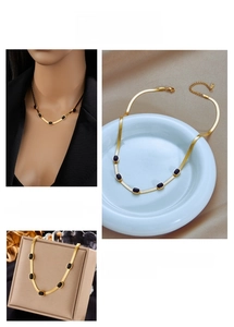 Detail view of gold snake chain necklace with black oval charms and lobster clasp