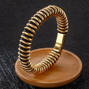 Detail of golden threaded bangle with black rubber accents on a wooden tray