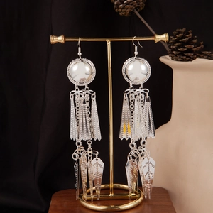 Detail of silver bohemian tassel earrings with geometric leaf pendants on a display stand