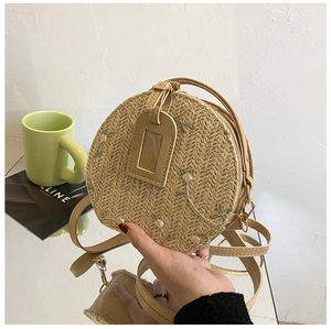 Detail of round straw crossbody bag featuring floral embroidery and leather tag accessories