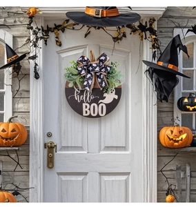 Detail of Halloween ghost BOO wooden sign with black ribbon and green plants on white door