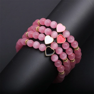 Pink cat eye stone beaded bracelets with heart charms on a black display stand