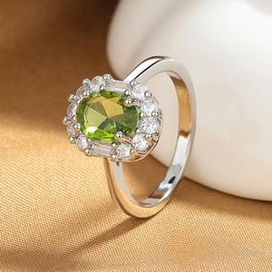 Close-up of silver ring with oval green gemstone and cubic zirconia on gold fabric