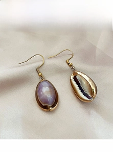 Macro detail of bohemian cowrie shell earrings with gold edges on satin fabric