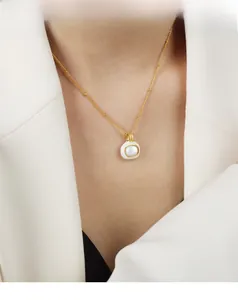 Detail of a square gold pendant with white shell inlay on a beaded chain necklace