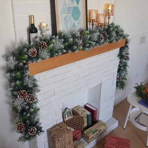 Lush snow-flocked Christmas garland with pine cones draped over a white stone fireplace