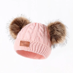 Close-up of pink knit baby hat with soft faux fur pom-poms and leather logo patch