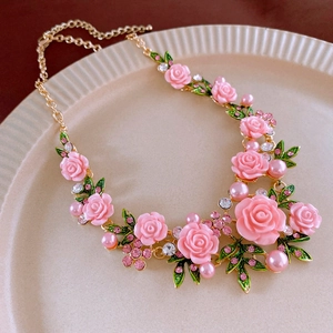 Close-up of pink resin rose flower necklace with green leaves and pearls on tray