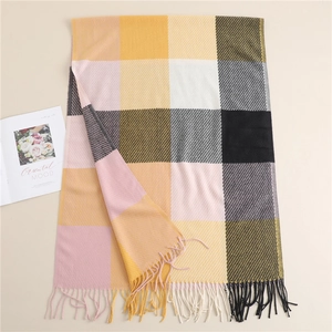 Flat lay of a large plaid scarf with yellow and pink tassels on a beige background