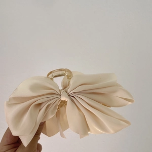 Detailed view of a large champagne satin bow hair claw clip held by hand for size