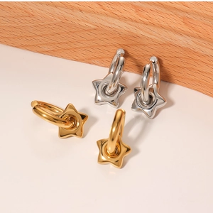 Detailed close-up of 18k gold and silver star charm hoop earrings on a wooden background