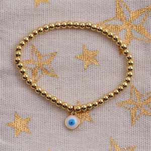 Detail view of gold bead bracelet with blue enamel evil eye charm on star pattern fabric
