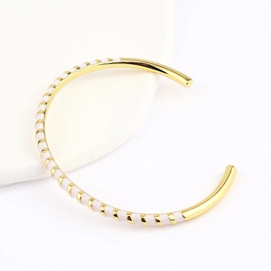 Detail of a gold-plated C-shaped cuff bracelet with white enamel stripe patterns
