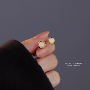 Macro view of S999 silver stud earring with cream round bead held by fingertips