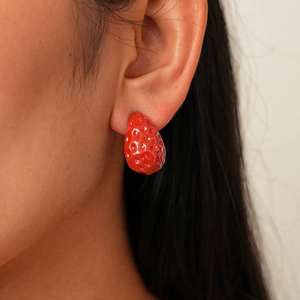 Close-up of a model wearing a glossy red strawberry stud earring with realistic texture
