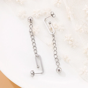 Macro detail of silver long tassel earrings with U-hook design on white lace fabric