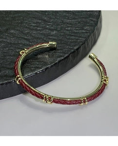 Dettaglio macro della pelle intrecciata rossa e finitura in metallo dorato del bracciale