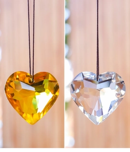 Detail of amber and clear heart crystal suncatchers with black lanyards on wood background