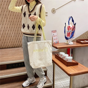 Detail of off-white canvas tote bag featuring yellow smile embroidery and woven straps
