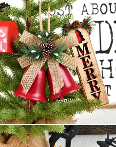 Close-up of red metal Christmas bells with a linen bow and MERRY wooden tag on tree