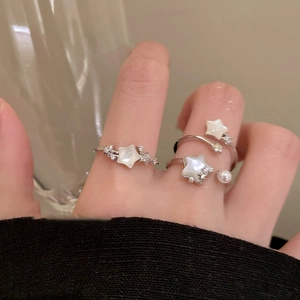 Close-up of silver star-shaped rings with sparkling zircon and pearl on model hand