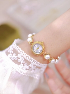 Detailed view of women's gold quartz watch with elegant white pearl bracelet on wrist