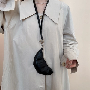 Gros plan d'un mini sac croissant noir en cuir PU porté sur un trench-coat beige