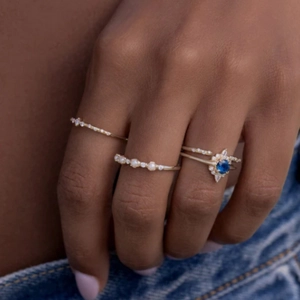Detail of stacked gold rings with blue gemstone, pearls and diamonds on denim background