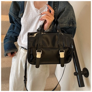 Detail of a black patent leather tote bag with silver metal buckles on marble stairs