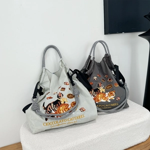 Detail of grey nylon tote bags featuring cat illustrations and side drawstring design
