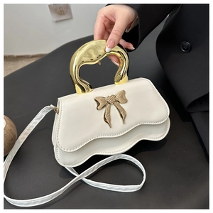 Detail of white wave-edge handbag with golden bow and liquid metal handle