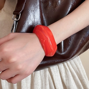 Detail view of a translucent red acrylic wide bangle worn on a wrist against a leather bag